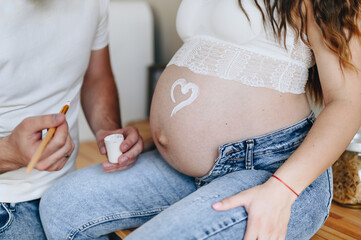 The concept of pregnancy, motherhood and health - a man draws a heart symbol on the belly of his pregnant wife