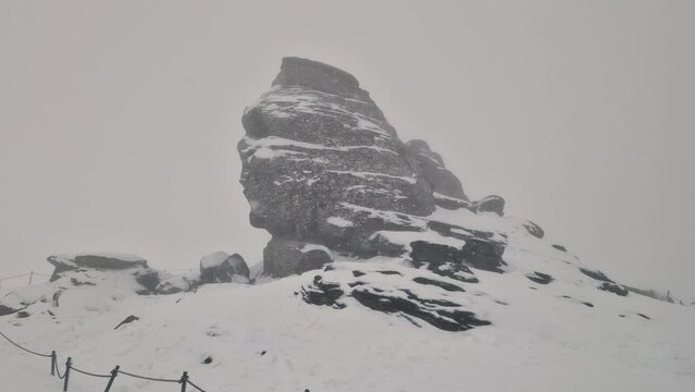 Handheld footage with the Sphinx (Sfinxul), a natural rock formation in the Bucegi Natural Park, in the Bucegi Mountains of Romania, during a snowy winter day.