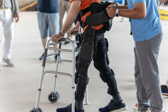 Boy with Mobility Problems in Lower Limbs in Upright Posture Walking Thanks to a Mechanical Exoskeleton and with the Help of his Physical Therapist