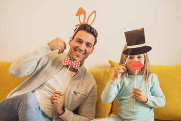 Father and daughter having fun with  party props at their home.