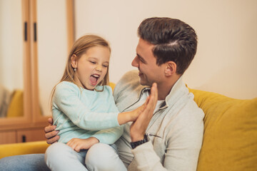 Happy father and daughter giving each other a high five at  their home.