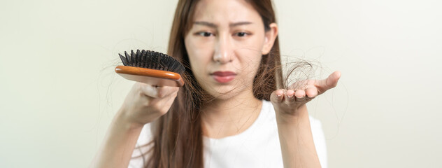 Serious, worried asian young woman, girl holding brush, show her comb, hairbrush with long loss hair problem after brushing, hair fall out on her hand in living room. Health care, beauty treatment.