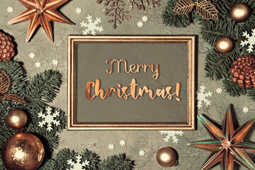 Christmas background. Flat lay with fir twigs decorated with red rowan berry, paper stars and snowflakes on grey green textured background. Greeting text Merry Christmas in frame.