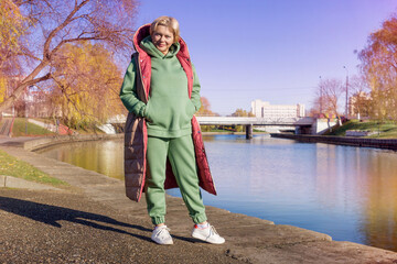 Mature woman on a walk in the autumn park in a green hoodie and long jacket, fashion.