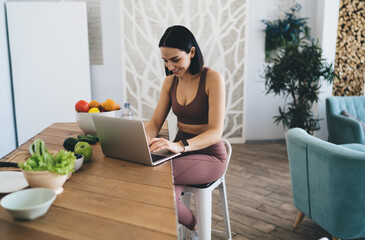 Happy woman typing on laptop while preparing healthy salad