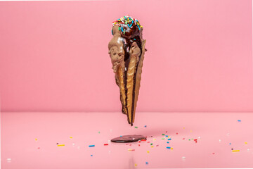 funny creative concept of flying wafer cone with ice cream covered, strewed sprinkles and poured with chocolate icing on pink background