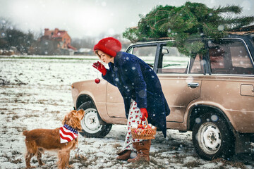 Christmas photo of a happy girl next to a retro car, a Christmas tree and an English Cocker Spaniel dog