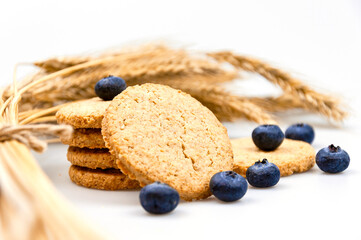 Cookies with bran and blue berries on a white background with rye ears.