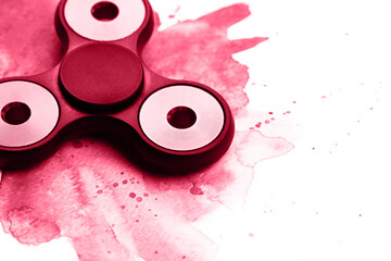 Black plastic beautiful spinner on watercolor background with splashes. Isolated on white background. Demonstrating Viva Magenta - trendy color of the year 2023