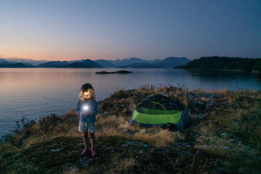 A young girl with a flashlight camping on a rocky island