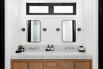 A cozy bathroom with a wood cabinet, marble countertop, and sconces around square mirrors.