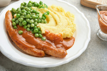 Bangers and mash. Grilled sausages with mash potato and green pea on white plate on grey background. Traditional dish of Great Britain and Ireland. BBQ beef sausages. Top view.