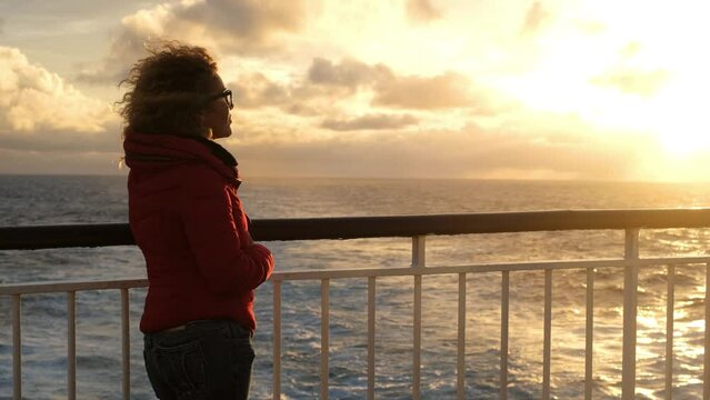 One lady with red winter warm jacket enjoy the sunset on the cruise boa deck during ocean travel, Transport and traveler people lifestyle. Tourist in winter sea holiday vacation day. People on ferry