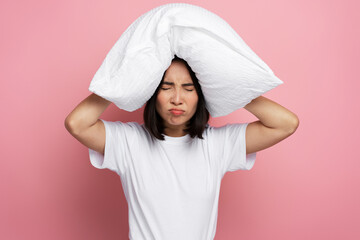 Nervous asian woman putting pillow at her head and feeling angry of loud neighbours