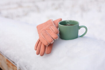 Obraz na płótnie Canvas Christmas background with gloves and hot tea on a snow-covered park bench. Selective focus.