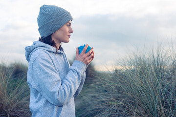 woman drinking coffee while looking at view wearing a wooly hat and hoodie. Staying warm while...