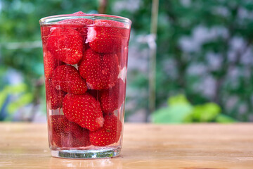 A glass glass filled with red strawberries and water standing on a wooden table