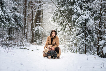 Portrait of a young beautiful girl with a Yorkshire terrier in the winter forest.