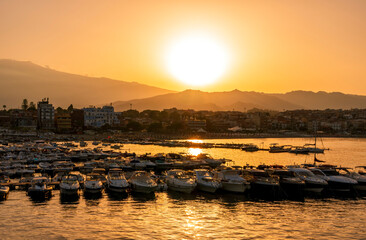 picturesque sunrise or sunset in a sea port with a gulf dock pier with tour boats and a town with cloudy sky on background of a seashore landscape