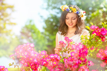 Fairy tale image art photo. Outdoor close up portrait of young beautiful happy smiling fantasy woman. Young goddess enjoys spring nature in bright sunlight and many pink roses