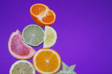 Fototapeta na wymiar Sliced citrus fruits in different sizes and colors close up on purple background 