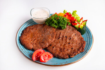 meat cutlets with sauce, fresh vegetables and herbs on a white background