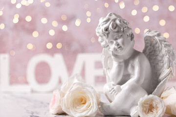 Little statue of white angle , white roses flowers  and word love against pink  textured wall. Selective focus. Place for text.