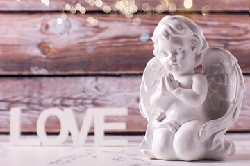 Little statue of white angle and word love  against brown textured wall. Selective focus. Place for text. St. Valentine day postcard.
