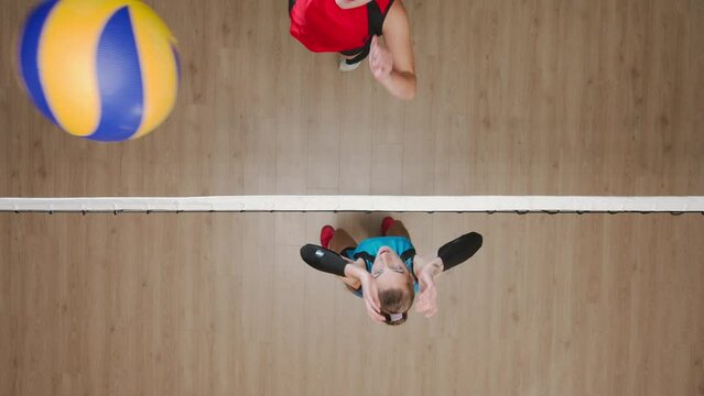 Two young female athletes playing volleyball on playground. Top view of volleyball player hitting the ball past the hands of blocker. Female players in blue and red uniforms.