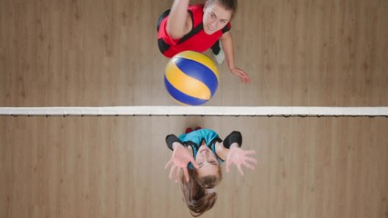 Two young female athletes playing volleyball on the playground. Top view of woman serving ball and an opponent hitting the ball and rejoicing in victory. Female players in blue and red uniforms.
