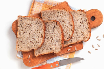 Wooden board with sliced whole grain bread and knife on a white background. Healthy bakery product. Top view.