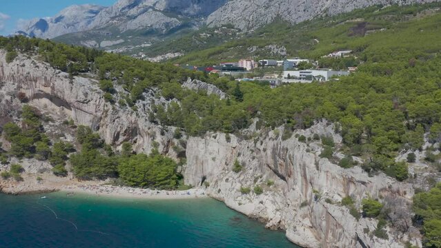 Beautiful beach among mountains and forest. Croatia. Makarska Riviera. Adriatic Sea lagoon with clear blue water and pine aroma. Drone video. Vacation . Many people. Nugal Beach