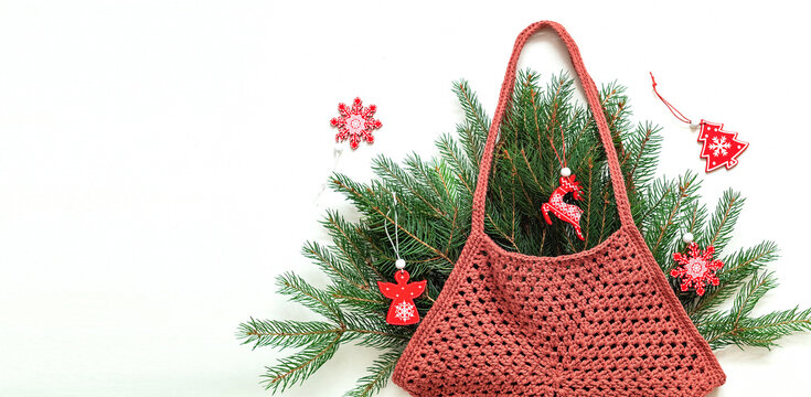 Burgundy crochet bag gexagon shaped with fir tree branches and Christmas wooden toys on a white background. Handmade shopping mesh bag. Copy space.