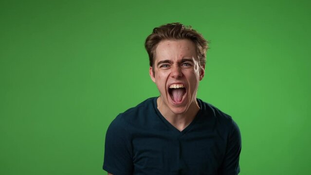Yelling angry frustrated despair upset with clenched fists portrait of young man 20s isolated isolated on green screen background in slow motion
