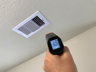 Measuring air conditioning flow temperature on a white ceiling register with a digital laser thermometer