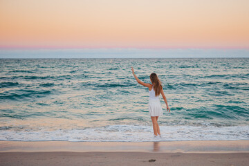 Fototapeta na wymiar Adorable happy girl on the beach at sunset walking in shallow water