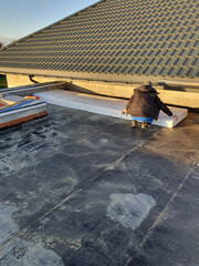 A man laying Styrofoam as insulation on the roof of a newly built house.