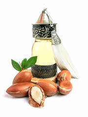 Argan oil in a oriental glass and metal bottle and argan nuts with green leaves isolated on white background.