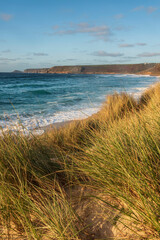 Fototapeta na wymiar Stunning landscape image of Sennen Cove in Cornwall during sunset viewed from grassy sand dunes with dramatic sky and long exposure sea motion