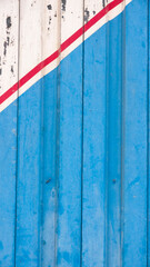 Puerta metálica deteriorada pintada de azul y blanco con líneas rojas