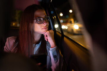 Business woman using smartphone while sitting in a backseat of a car at night