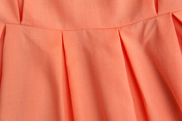 Part of skirt or dress is pale pink shade close-up. Peach clothing in fold of bright color, texture background