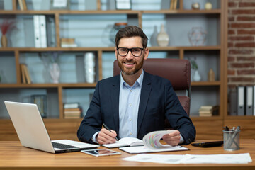 Portrait of successful and happy mature financier, senior businessman with beard and glasses smiling and looking at camera, man working inside office on paper work, investor satisfied with result.