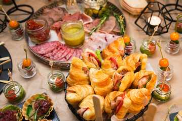 Croissant sandwiches with ham, iceberg lettuce, and tomato slices and sliced sausages, prosciutto, and bacon with mustard sauce