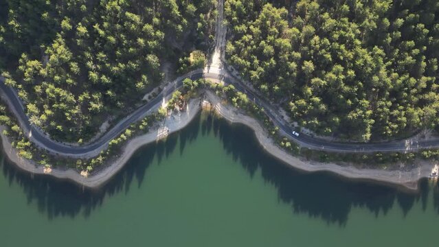Drone view of car driving on forest road by lake