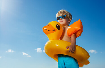Low angle portrait of boy with inflatable yellow duck buoy