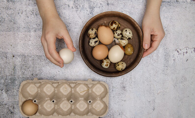 hands of invisible person carry fresh chicken and quail eggs from brown clay plate to egg tray. gray table. top view. High quality photo