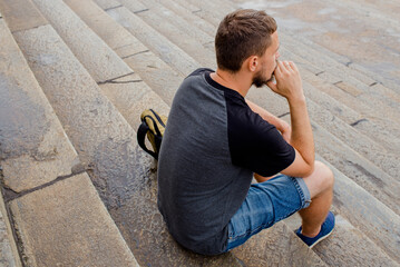 Man sits on the stairs and thinks emotionally. Close-up portrait of a young bearded man sitting on the steps
