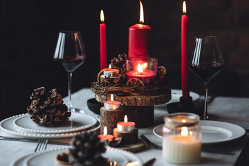 Rustic table decor for Christmas or New Year family dinner. Centrepiece with red candle, dry orange, cone, cinnamon, anise. Zero waste eco-friendly home. Cozy atmosphere, dark background. Close up