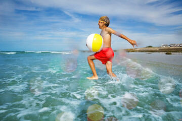 Cute boy run with inflatable ball in ocean at the beach